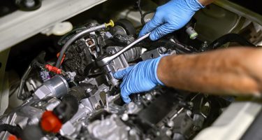 Hands of a mechanic wearing blue gloves working on a car engine with a spanner in a concept of maintenance and repair